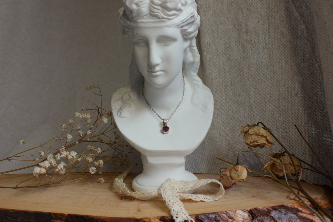 Présentation d'un collier artisanal avec un pendentif en tourmaline posé sur un buste en plâtre blanc, entouré de fleurs séchées, pour illustrer l'article de blog "Guide pour choisir son bijou".