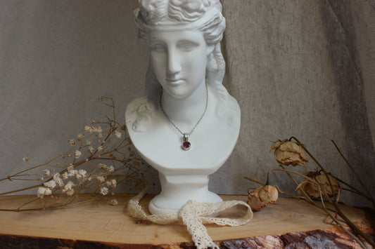 Présentation d'un collier artisanal avec un pendentif en tourmaline posé sur un buste en plâtre blanc, entouré de fleurs séchées, pour illustrer l'article de blog "Guide pour choisir son bijou".